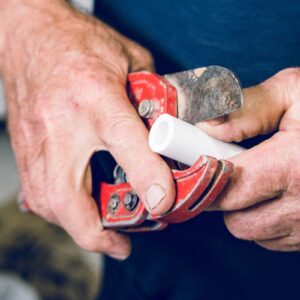 A person's hands use red pipe cutters to trim a white PVC pipe