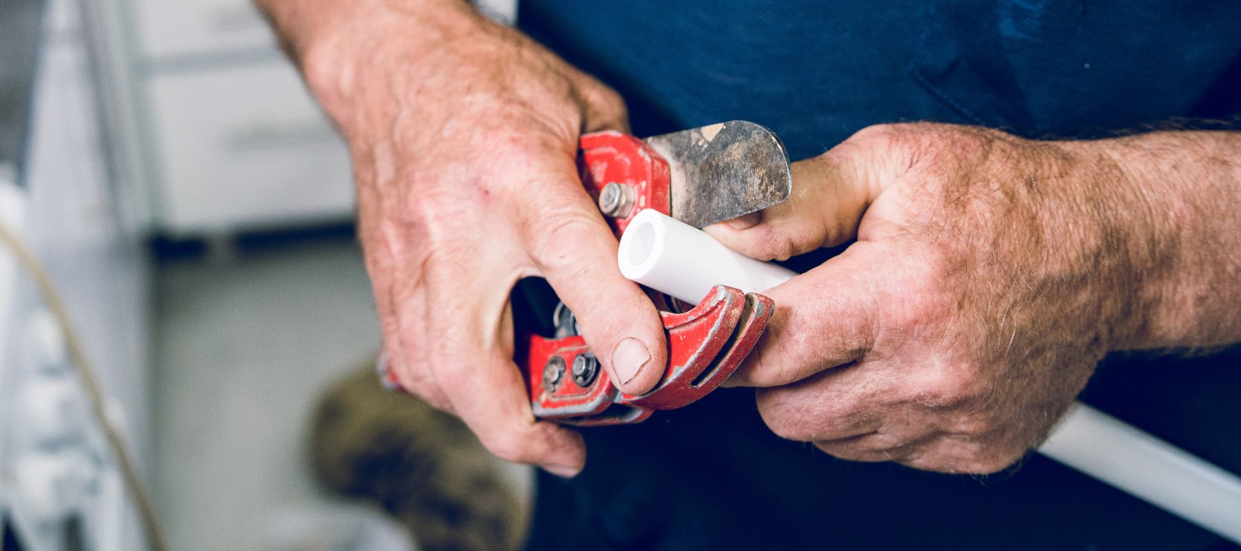 A person's hands use red pipe cutters to trim a white PVC pipe