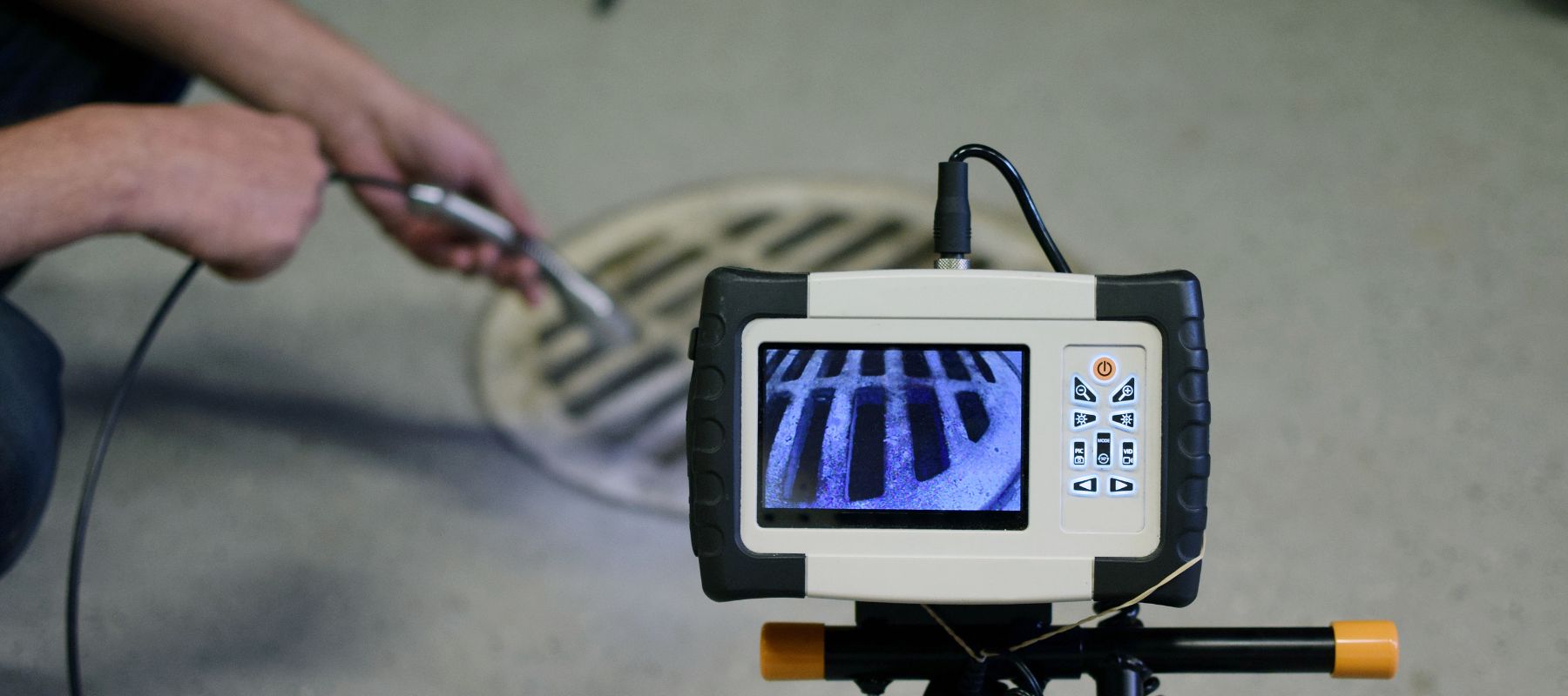 A technician monitors a screen displaying a view from a sewer camera, with a manhole cover in the background