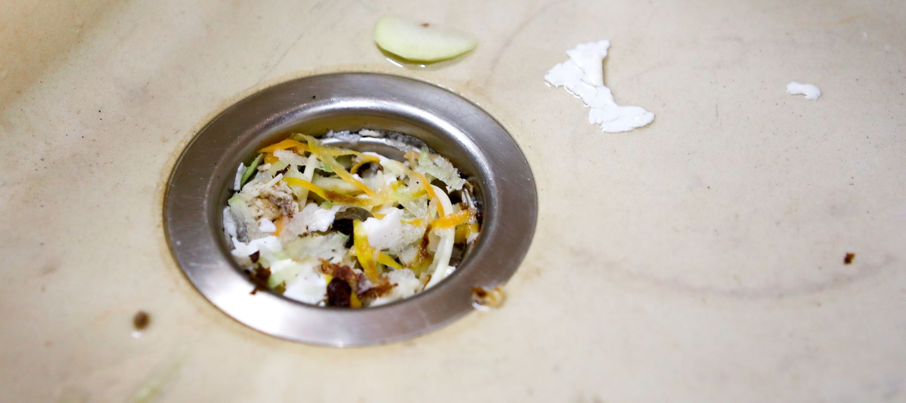 A kitchen sink drain is partially clogged with food scraps and debris