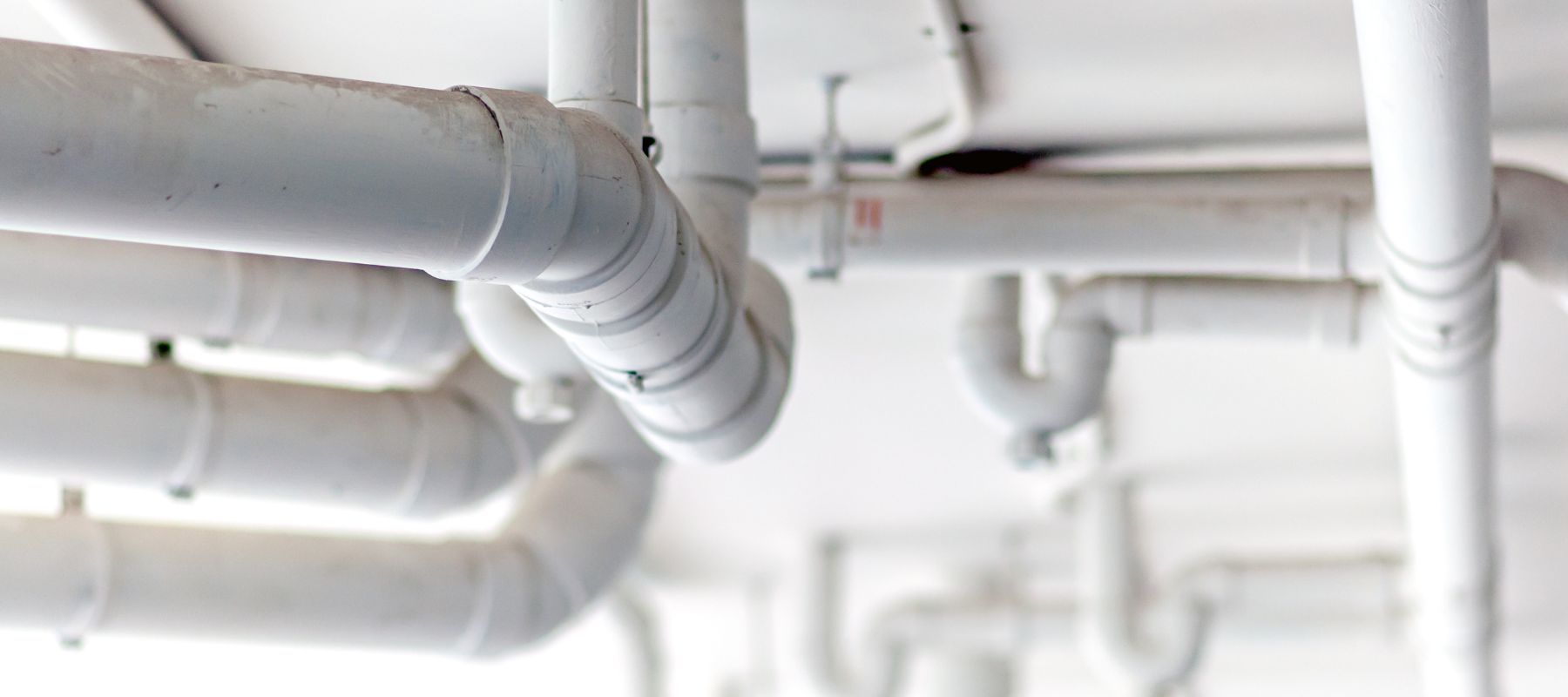 A network of white PVC pipes runs along a ceiling, some curving and connecting