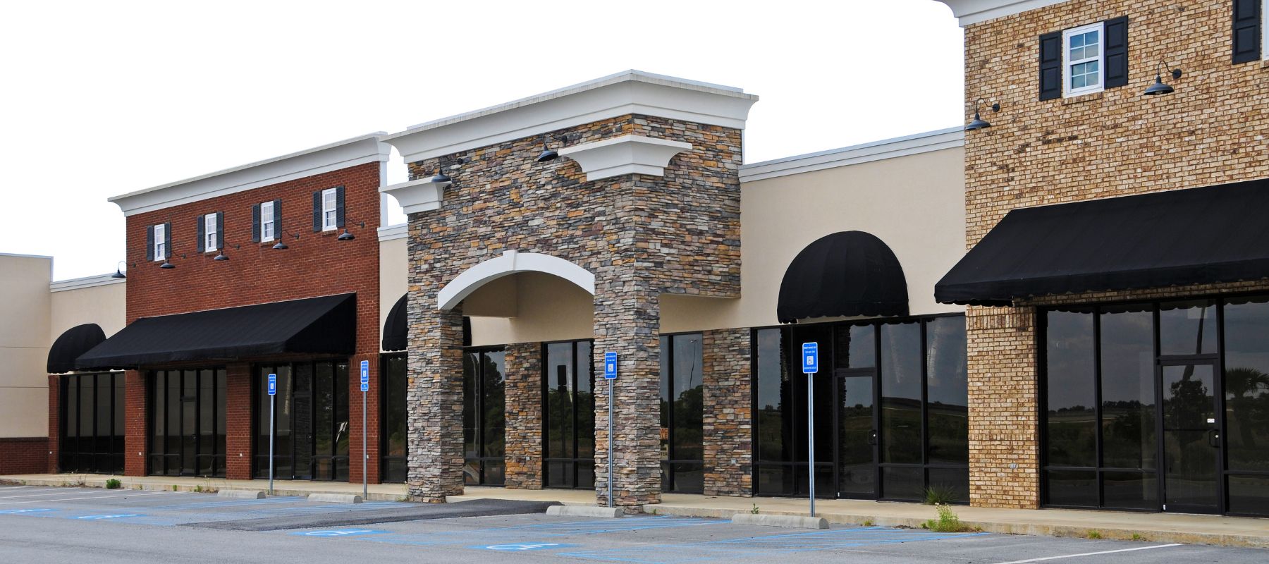 A row of vacant commercial storefronts with brick and stone facades features black awnings and empty windows