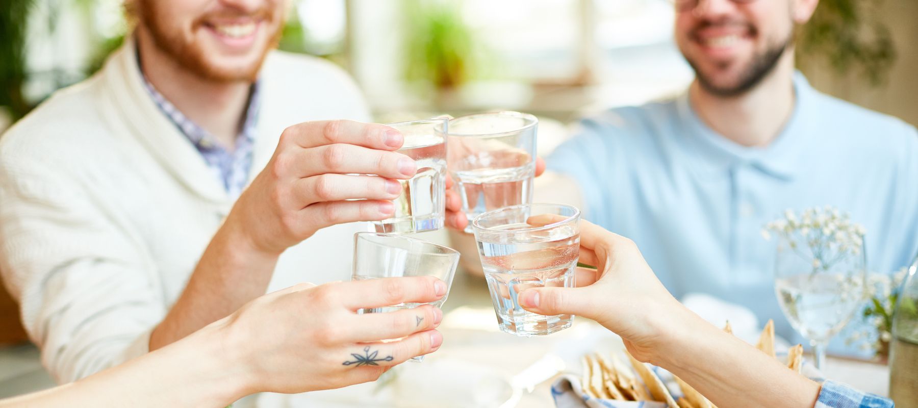 Four people are making a toast with glasses of water around a table, with food in the foreground