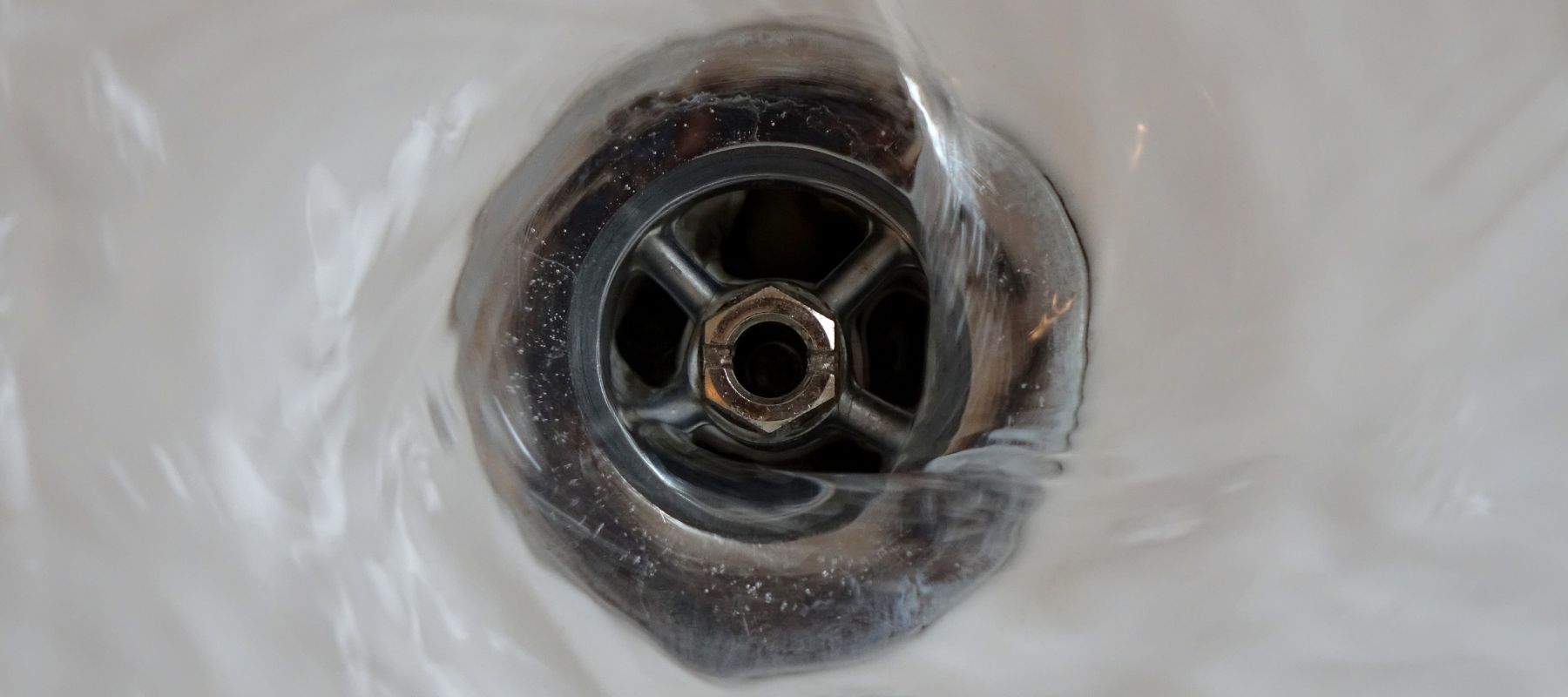 Water swirls down a chrome sink drain, creating ripples in the white basin