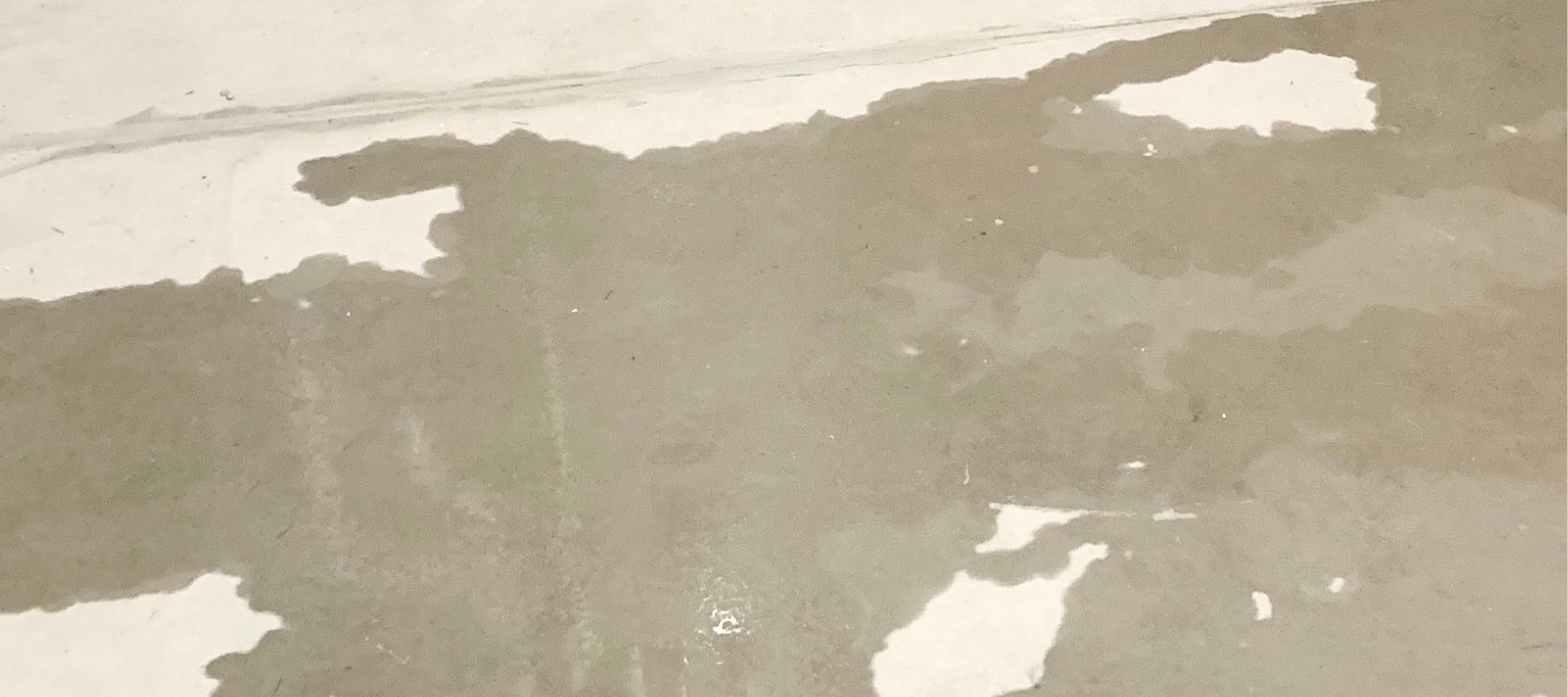 A large, irregular wet stain spreads across a light-colored concrete or tiled floor