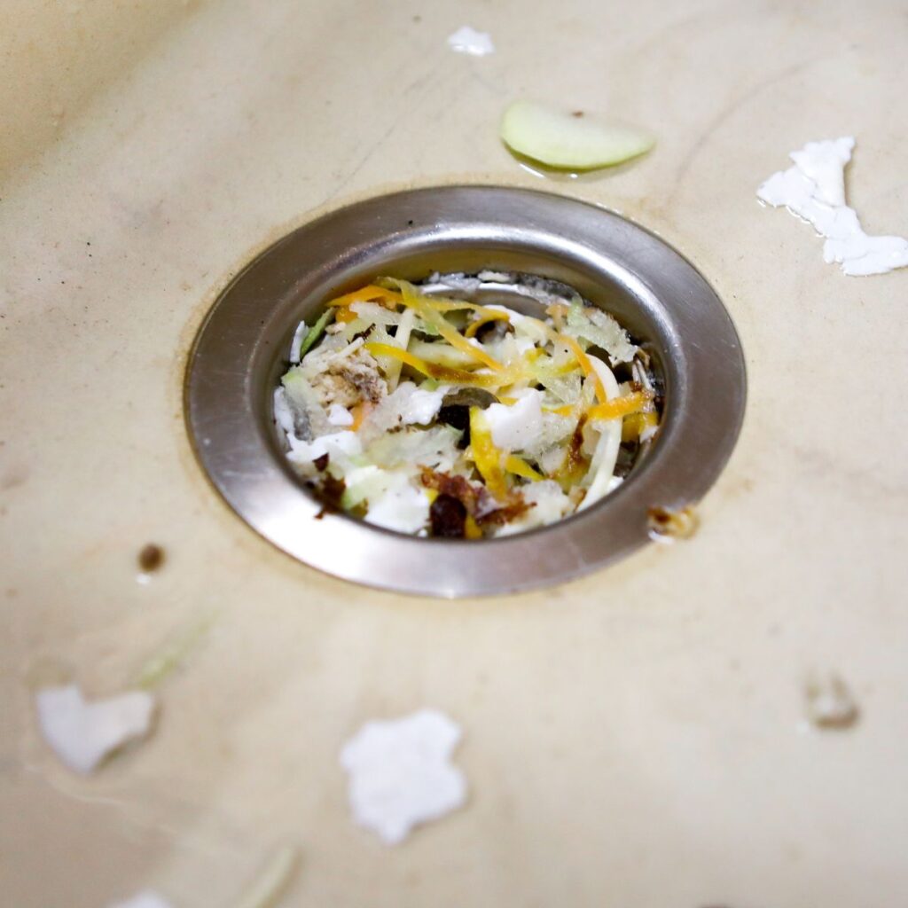 a kitchen sink drain is partially clogged with food scraps and debris