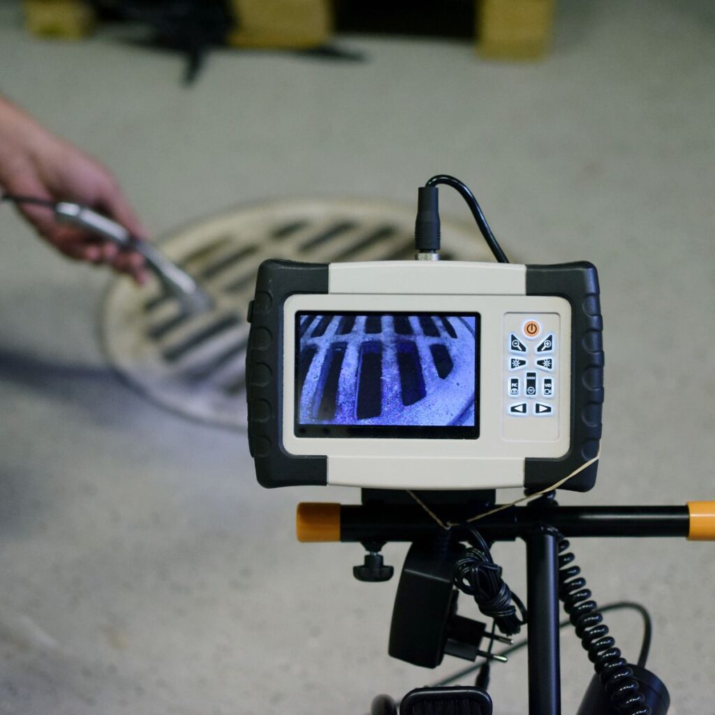 A technician monitors a screen displaying a view from a sewer camera, with a manhole cover in the background