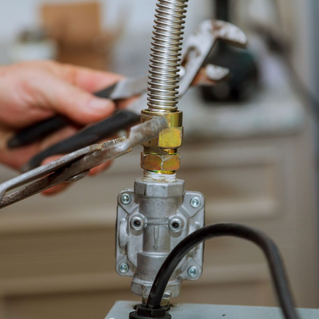 A person's hands use two wrenches to tighten a connection on a flexible corrugated metal gas line