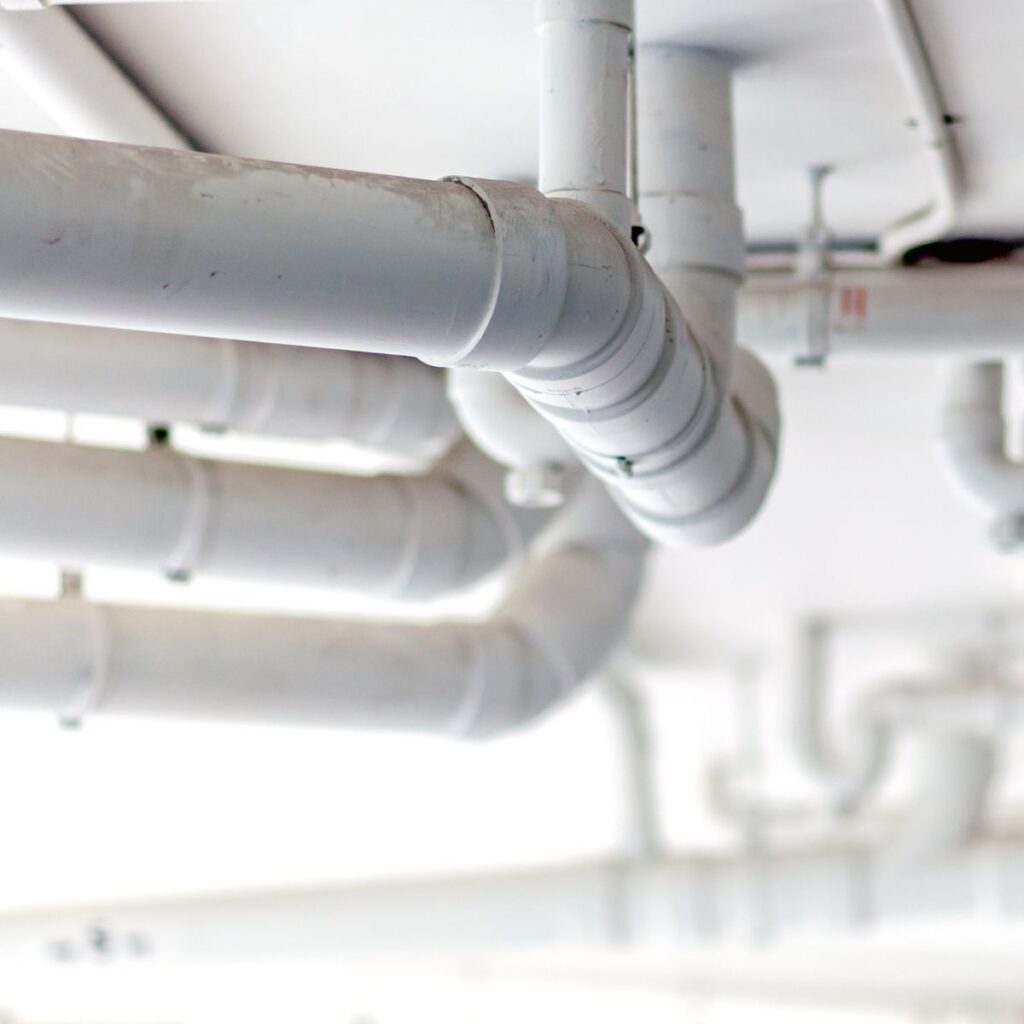 A network of white PVC pipes runs along a ceiling, some curving and connecting